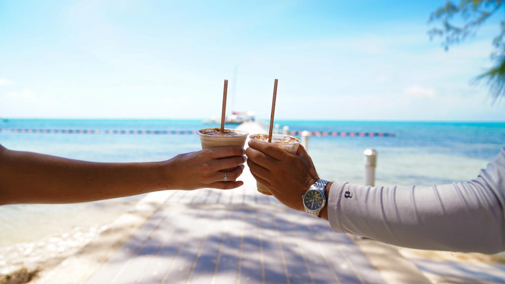 A man and woman hand holding 2 mudslides by the Caribbean beach
